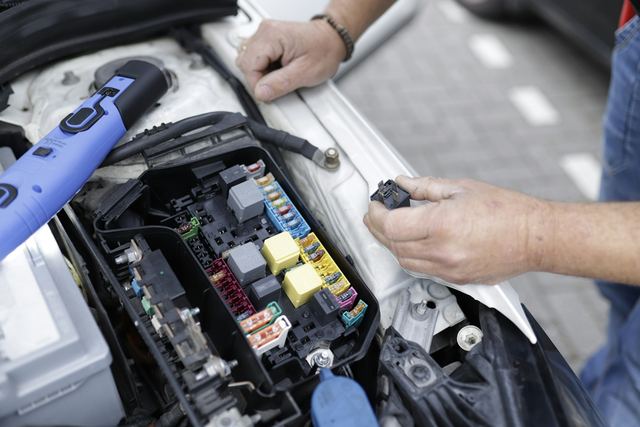 Twee handen werken aan de zekeringkast onder de motorkap
