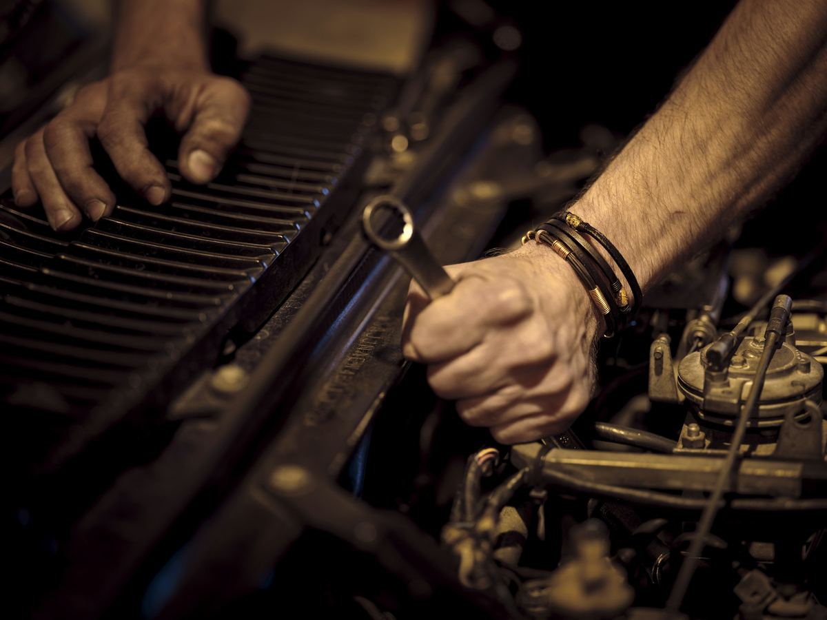 Twee handen met een steeksleutel aan een motorblok, in warm licht