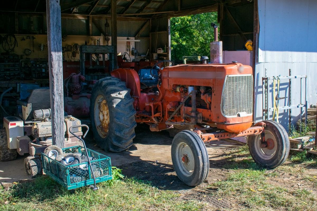 Een oude oranje tractor in een open loods met gereedschap aan de wand