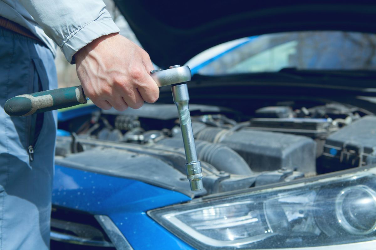 Een hand draait met een ratelsleutel aan de motor van een blauwe wagen